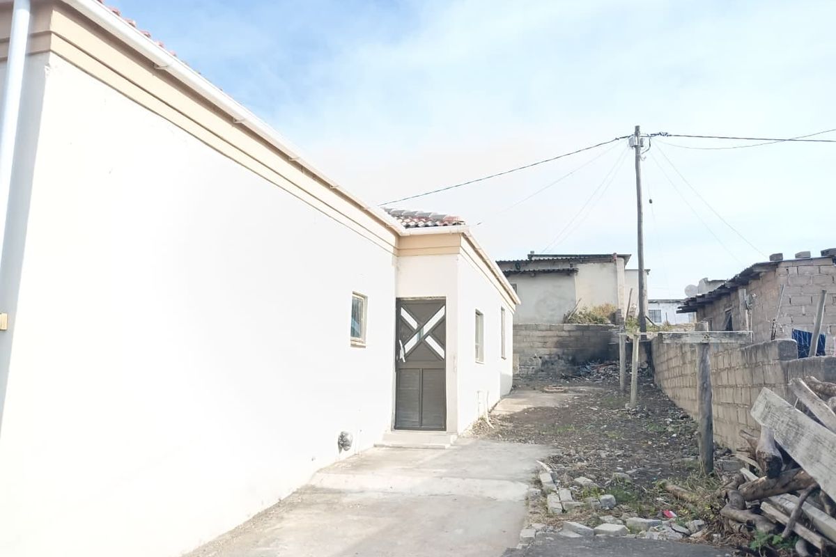Rear exterior view of the property featuring a concrete pathway, external door, and a basic yard area with boundary walling.