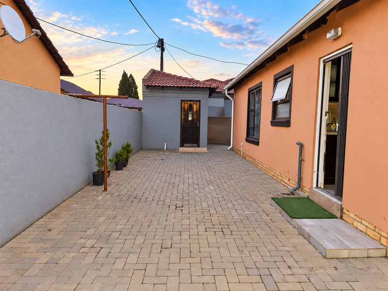 A paved rear courtyard area featuring a boundary wall, security gate, and access to the main dwelling and outbuilding.