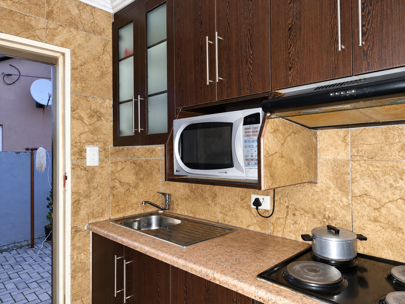 A functional kitchen featuring dark wood cabinetry, a stainless steel sink, built-in microwave, extractor fan, and electric hob with tiled splashback finishes.