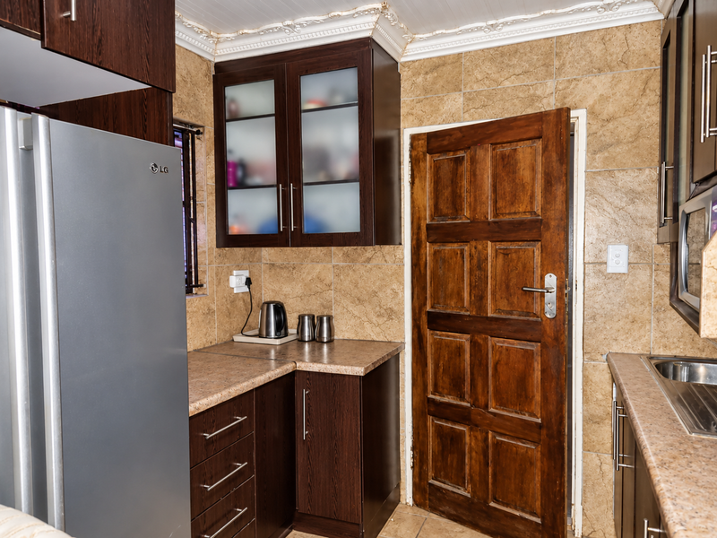 A functional kitchen featuring dark wood-look cabinetry, stone-effect tiled walls, and a classic solid wood door, offering a traditional aesthetic.
