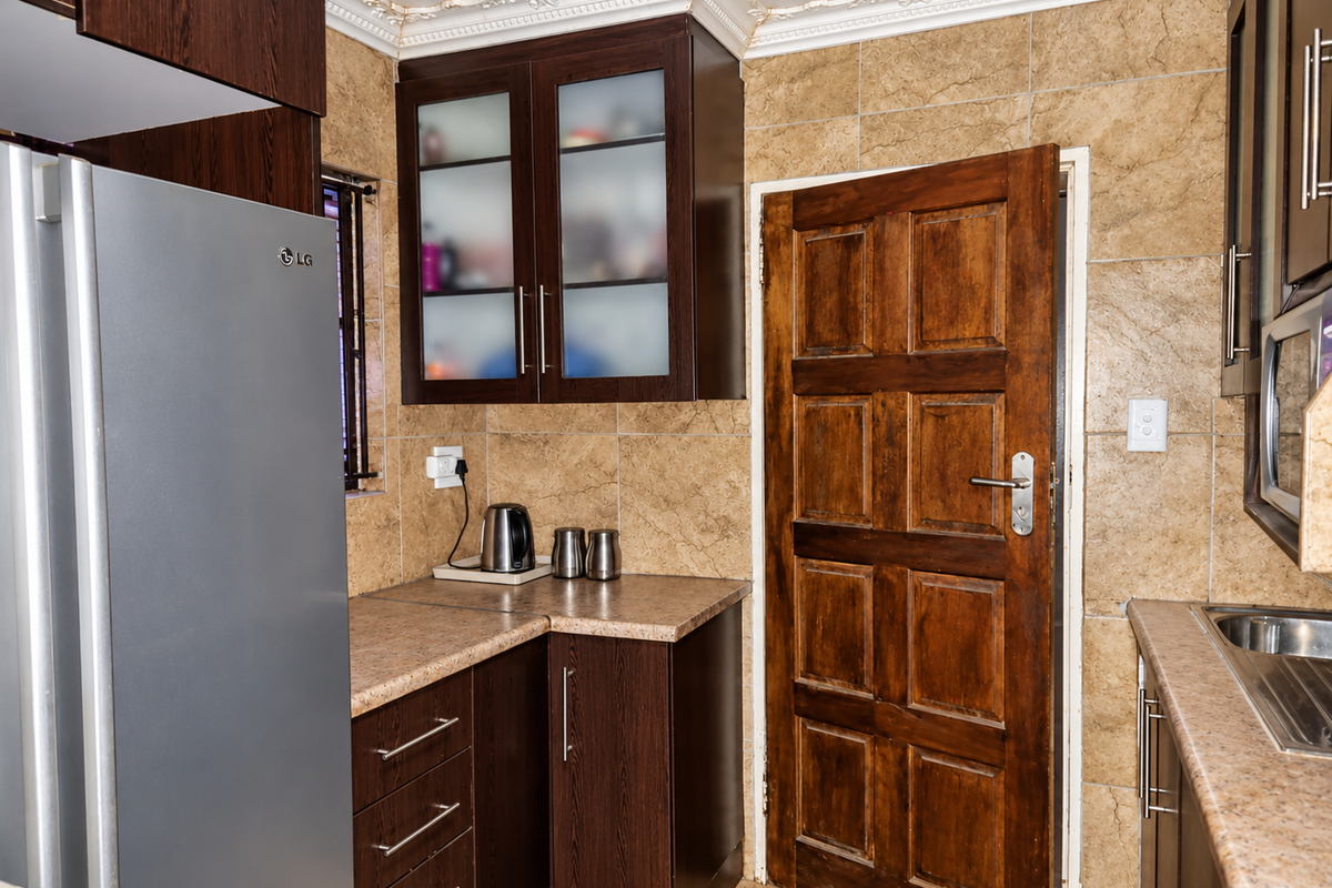 A functional kitchen featuring dark wood-look cabinetry, stone-effect tiled walls, and a classic solid wood door, offering a traditional aesthetic.