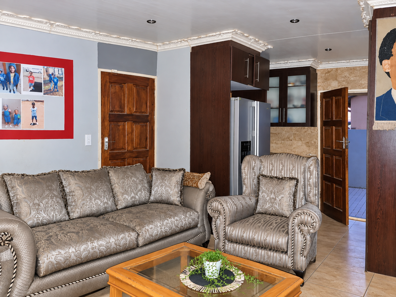 Open plan living area featuring tiled floors, decorative ceiling cornices, recessed lighting, and direct access to an adjacent kitchen and exterior space.
