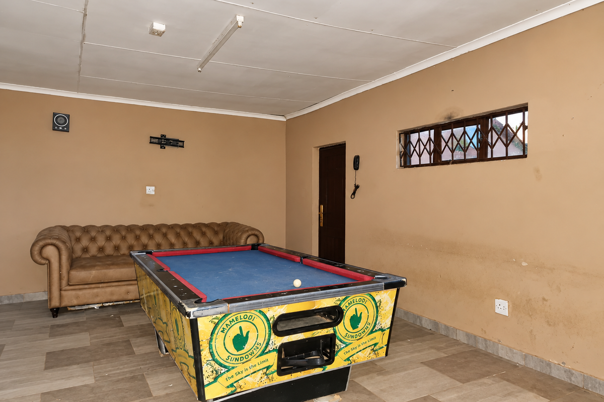 A multi-purpose living area featuring tiled flooring, security-barred windows, and basic lighting, currently utilized as a recreational space.