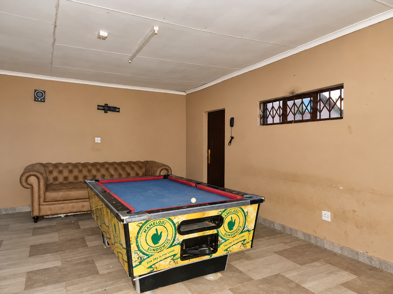 A multi-purpose living area featuring tiled flooring, security-barred windows, and basic lighting, currently utilized as a recreational space.