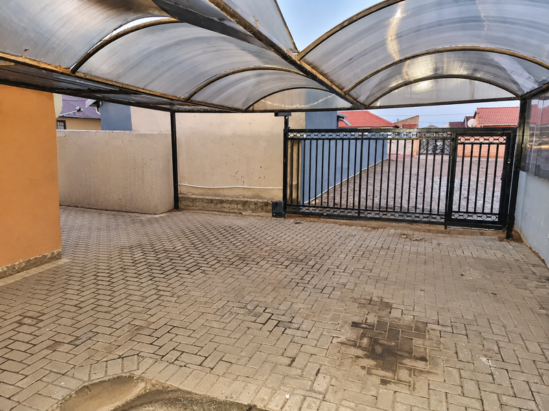A covered parking area featuring a durable polycarbonate roof canopy, paved driveway, and a secure metal gate entrance.