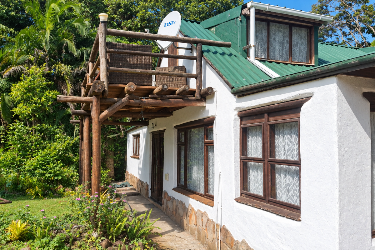Rear exterior view of the house featuring a timber balcony, corrugated metal roof, and stone cladding accents set against a lush garden.