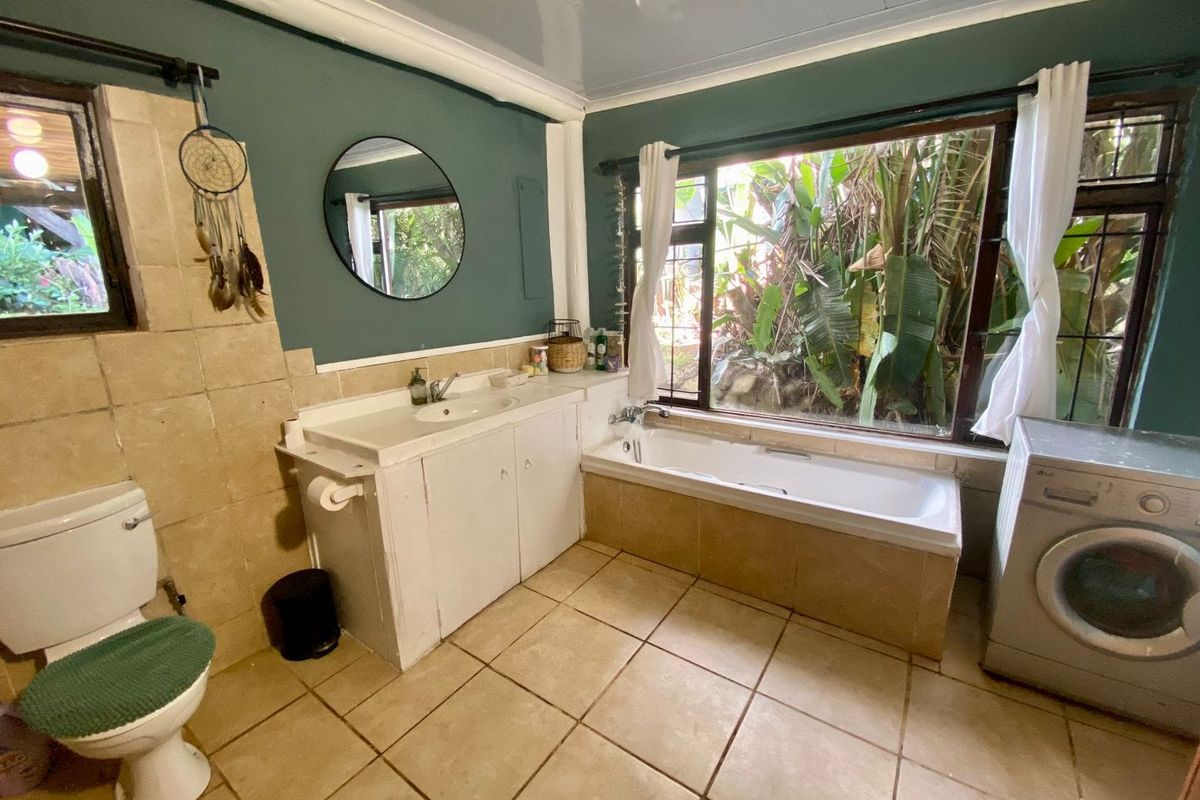 A functional bathroom featuring a built-in vanity, drop-in bathtub, and ceramic tile flooring, with large windows providing natural light and garden views.