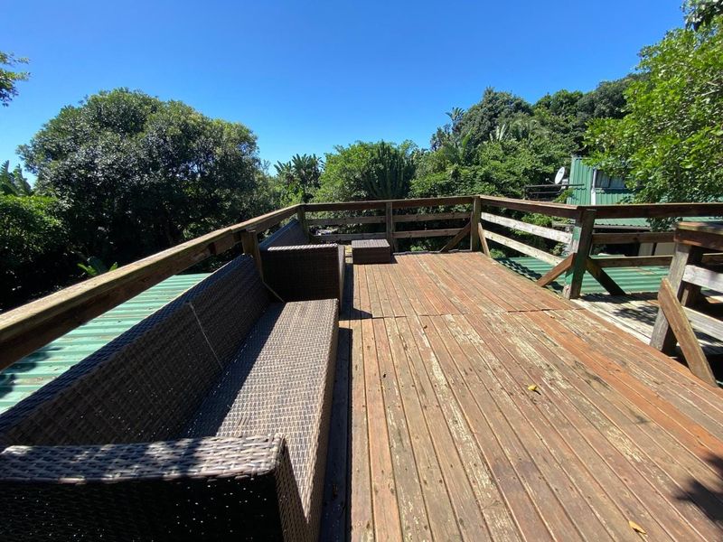 An elevated timber deck balcony featuring a wooden balustrade and views of the surrounding trees, requiring maintenance to the timber surface.