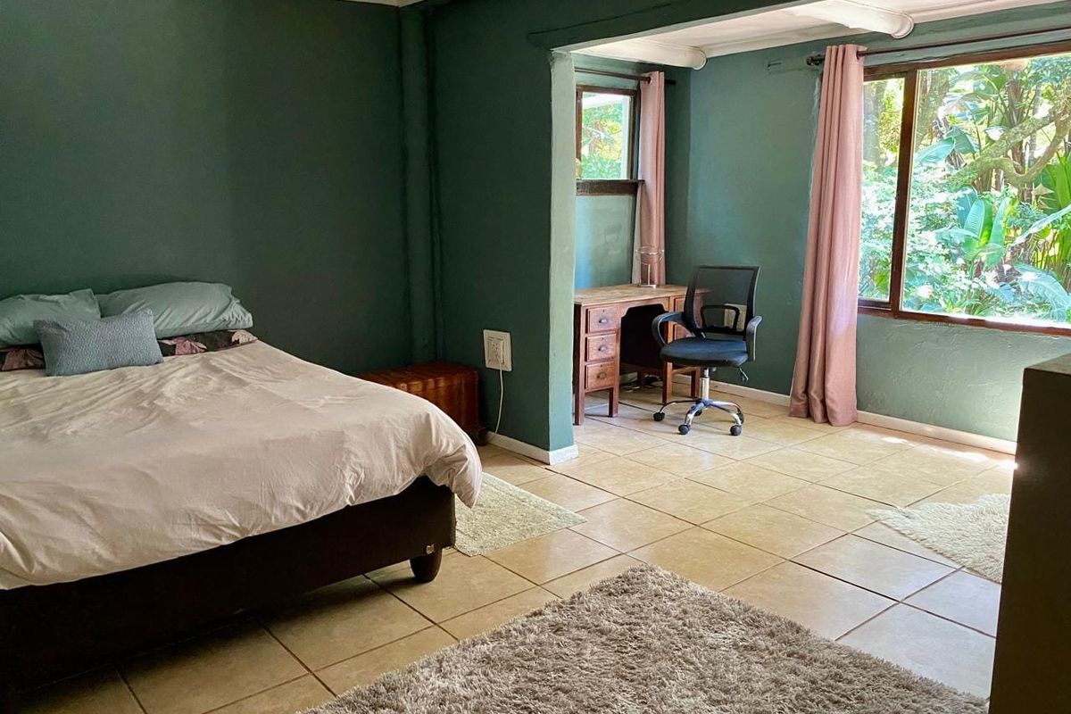 Spacious bedroom featuring tiled flooring, large windows with garden views, and a dedicated alcove area suitable for a home office setup.