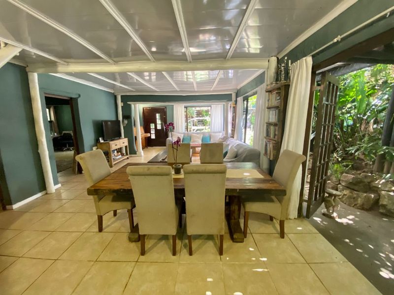 Spacious open-plan living and dining area featuring tiled floors, exposed beam ceilings, and direct access to the garden through french doors.