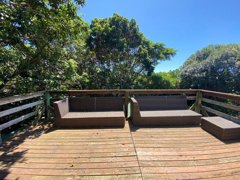 An elevated outdoor timber deck featuring a wooden balustrade, surrounded by mature trees, providing a private and natural outdoor entertainment space.