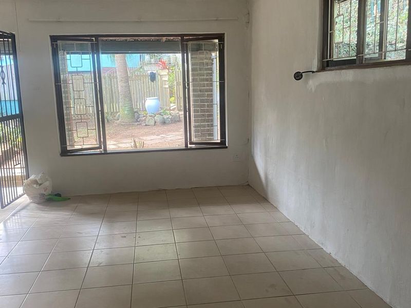 An empty, neutrally painted living room featuring tiled flooring, security bars on the windows, and a sliding door leading to the garden.