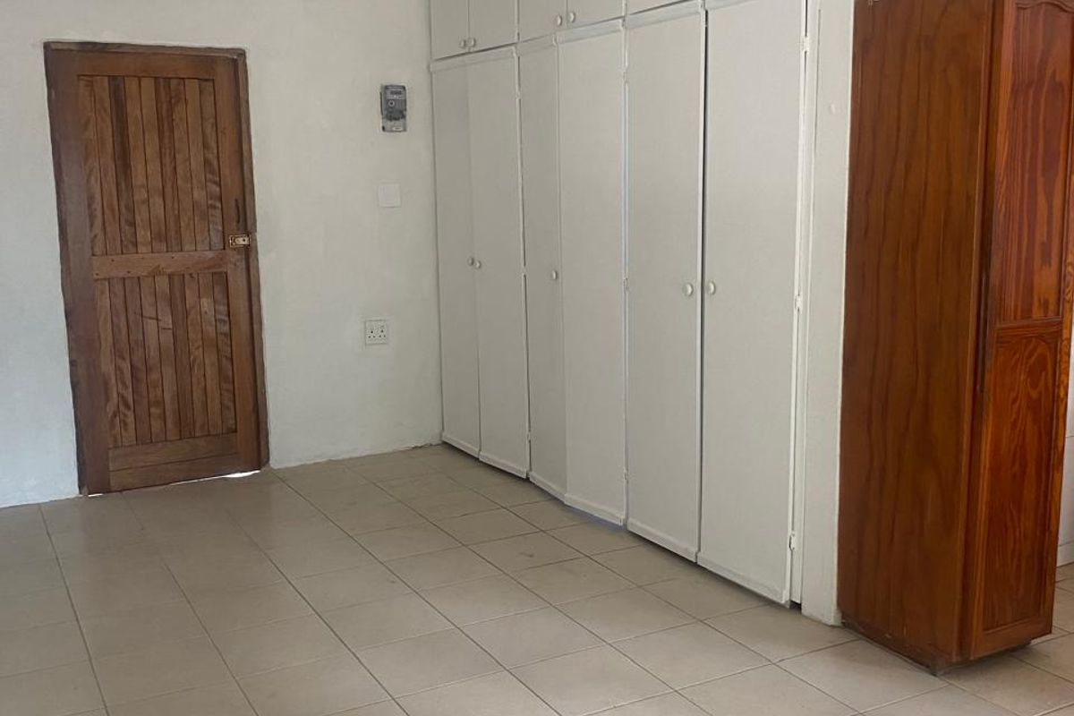 A spacious bedroom featuring tiled flooring, extensive built-in cupboard storage, and a classic wooden door, offering a functional blank canvas for personalization.