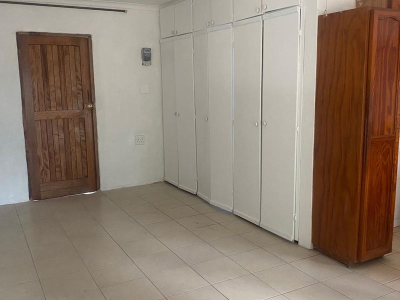 A spacious bedroom featuring tiled flooring, extensive built-in cupboard storage, and a classic wooden door, offering a functional blank canvas for personalization.
