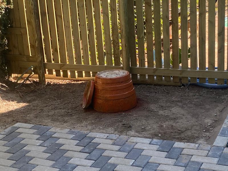 Rear garden area featuring a timber picket fence and a paved patio section, currently with an unlandscaped soil area requiring attention.