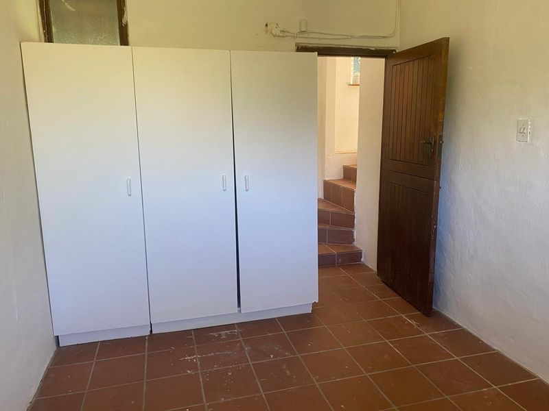A simple bedroom featuring built-in cupboards, tiled flooring, and a wooden door leading to a staircase.