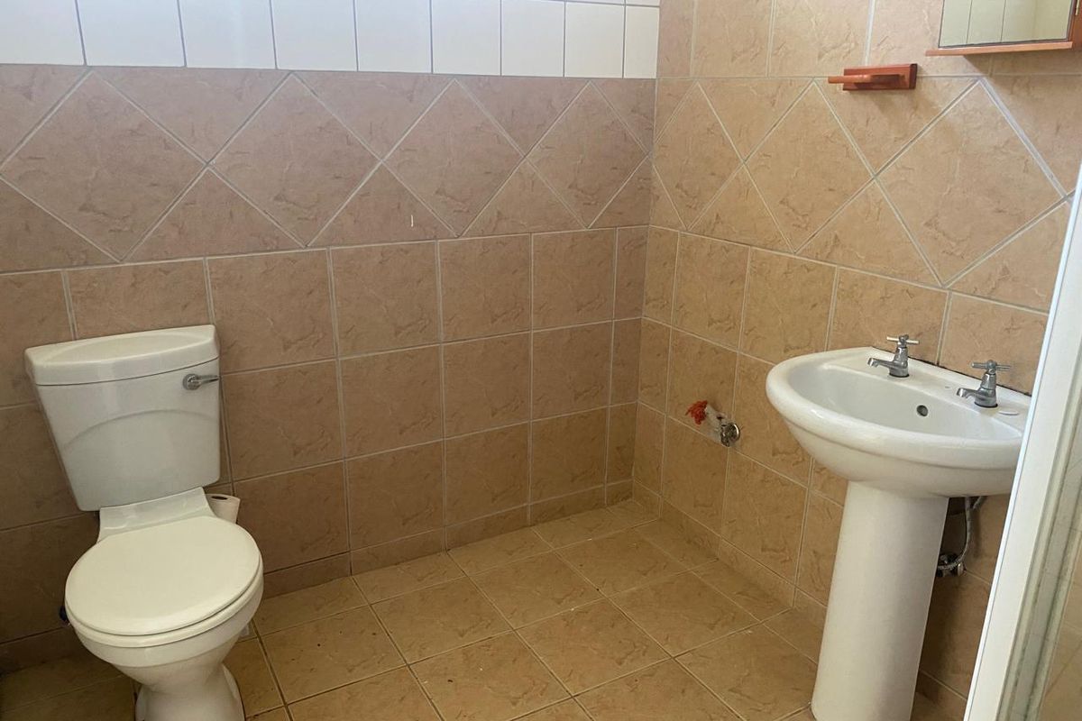 A functional bathroom featuring a pedestal basin and ceramic toilet with neutral tiled walls and flooring.
