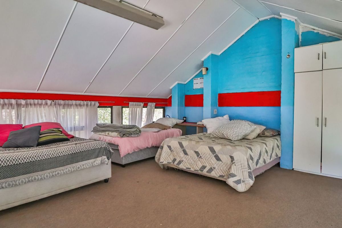 Spacious attic-style bedroom featuring a pitched ceiling, built-in wardrobe, and carpeted flooring, currently configured with multiple beds.