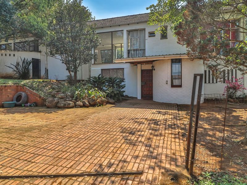 Front elevation of a multi-level house featuring a brick paved driveway, established garden, and traditional architectural design with a timber entrance door.
