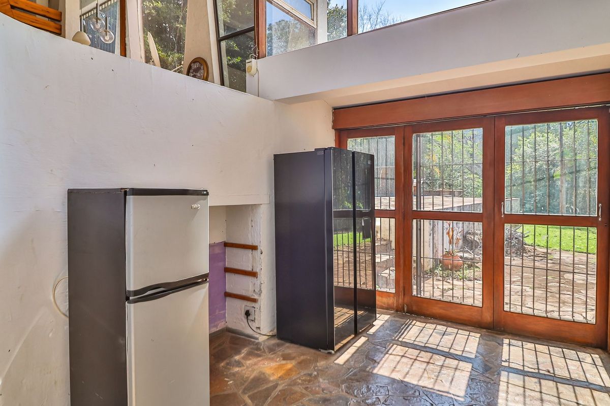 A kitchen area featuring stone flooring, timber-framed glass doors with security bars, and high-level clerestory windows providing natural light.