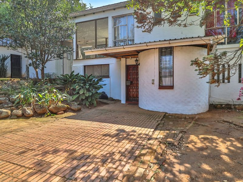 Front elevation of a unique multi-level home featuring a curved wall design, brick paved entrance, and established garden surroundings.