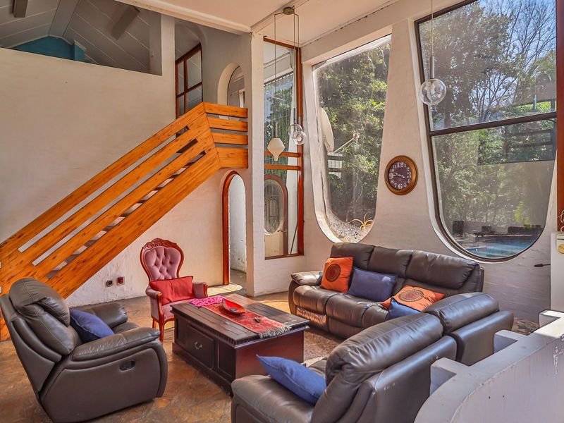 Spacious living room featuring a unique wooden staircase, vaulted ceilings, and large arched windows that provide ample natural light and garden views.