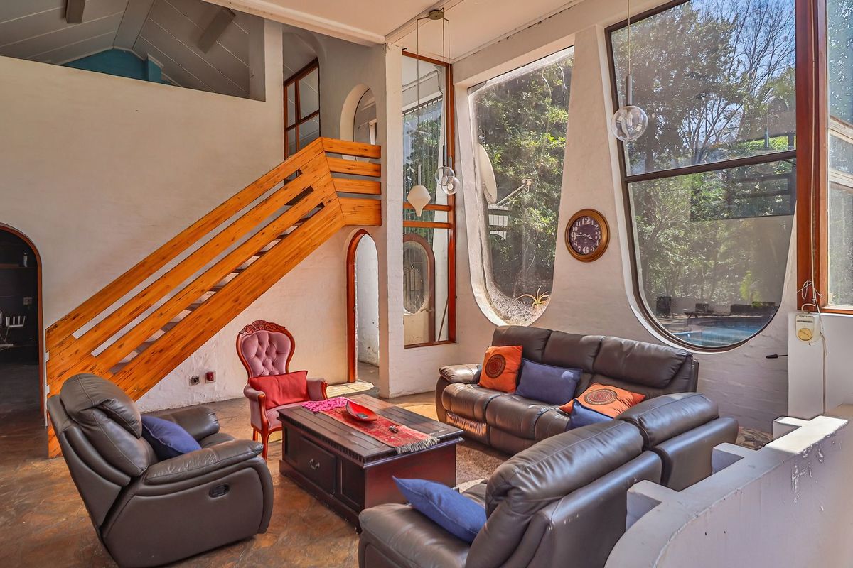 Spacious living room featuring a unique wooden staircase, vaulted ceilings, and large arched windows that provide ample natural light and garden views.