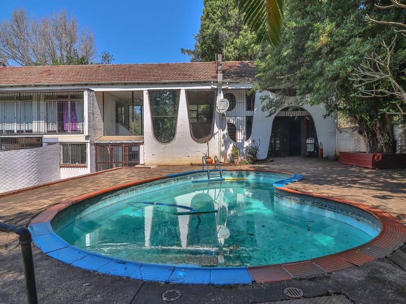 Rear exterior view featuring a swimming pool with surrounding paved patio area and unique arched architectural details on the main house facade.