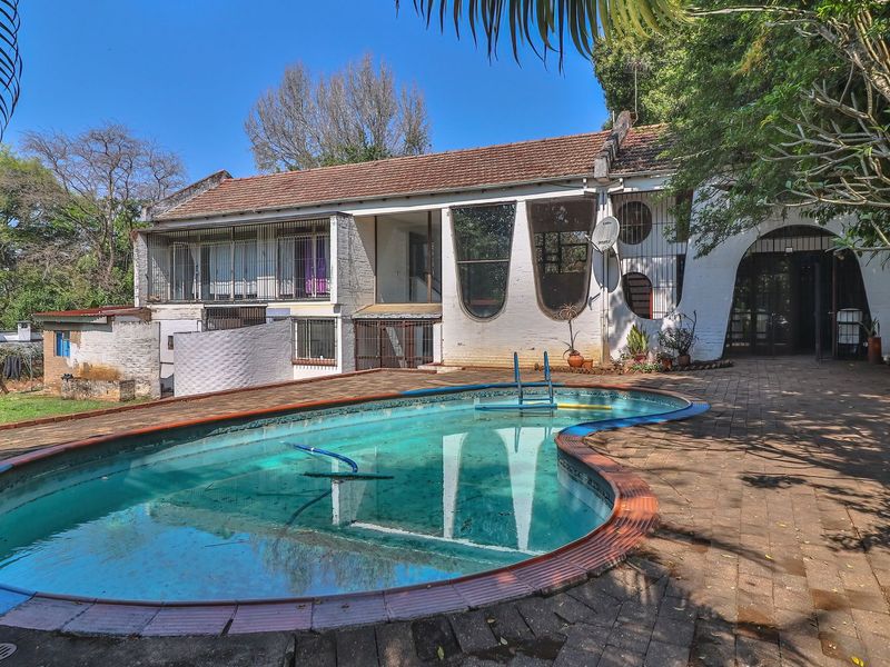 Rear exterior view featuring a swimming pool with paved surround and a multi-level house structure with unique arched window detailing.