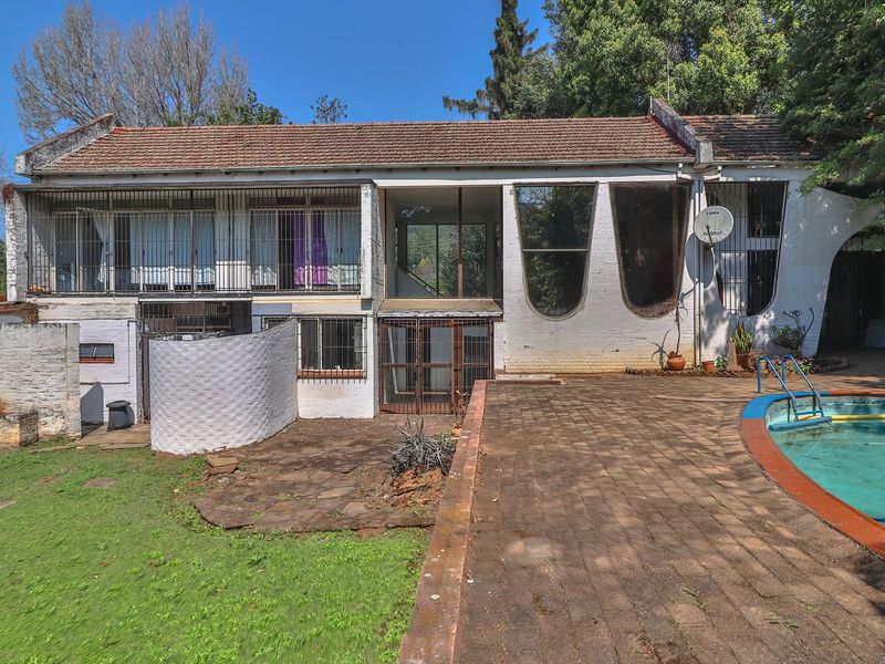 Rear exterior view of the property featuring a swimming pool, paved patio area, and a multi-level brick structure with security bars.