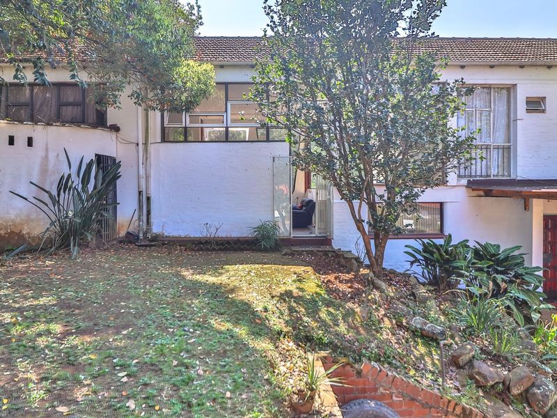 Rear elevation of the house featuring a multi-level facade, tiled roof, and established garden with brick retaining elements.