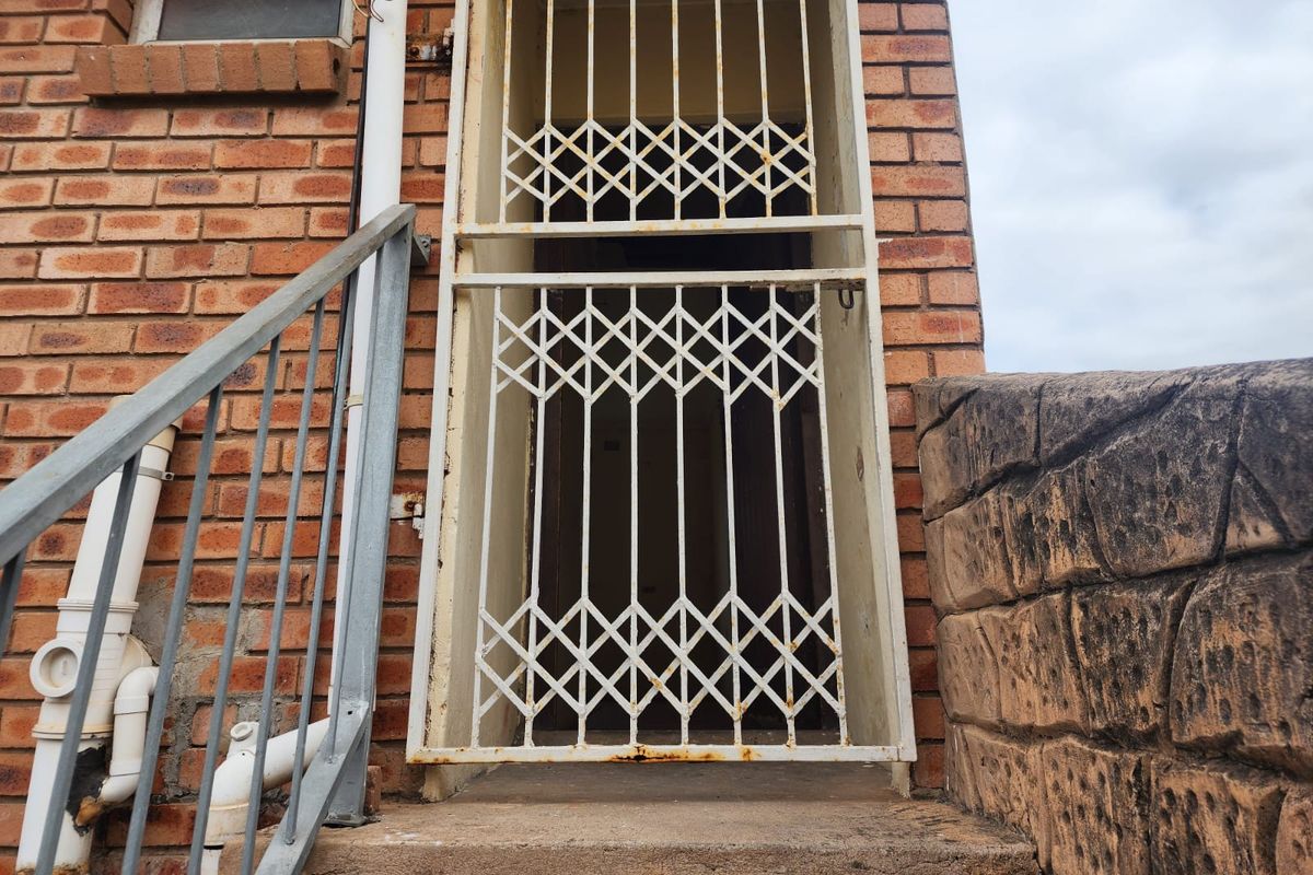 Exterior entrance featuring a brick facade, concrete steps, and a metal security gate with visible signs of weathering and rust.