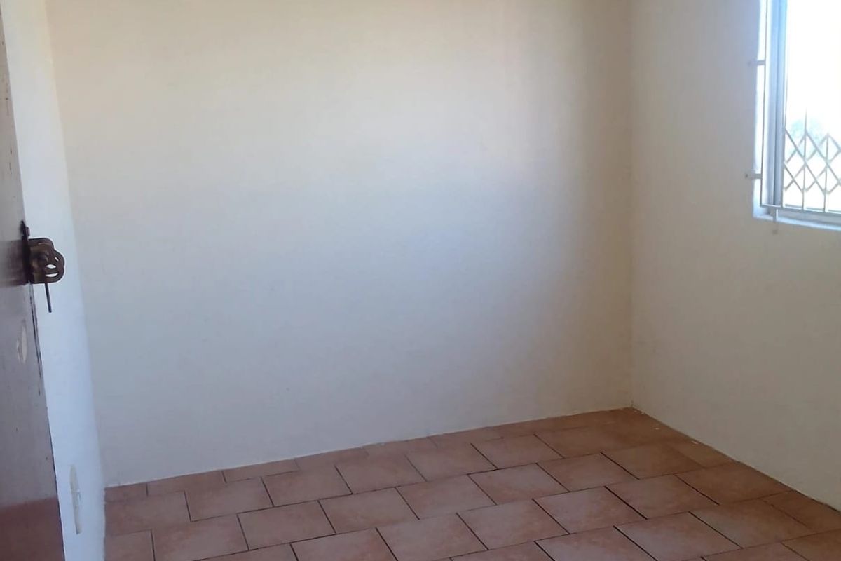 An empty bedroom featuring tiled flooring and a window with a security gate, providing a blank canvas for potential interior design.