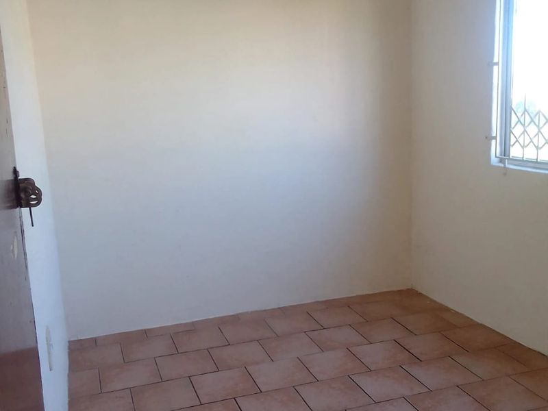 An empty bedroom featuring tiled flooring and a window with a security gate, providing a blank canvas for potential interior design.