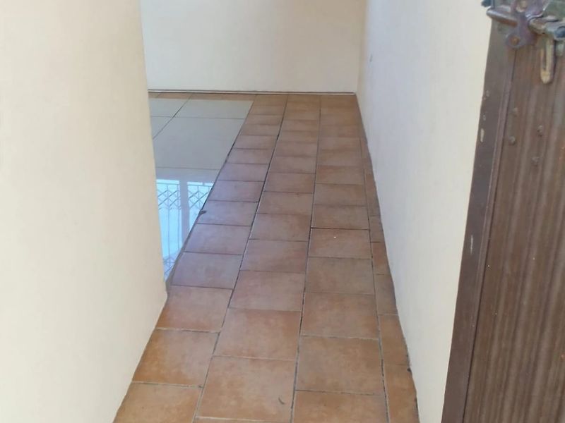 A vacant hallway featuring ceramic floor tiles and a wooden entrance door, leading into an adjacent living space.