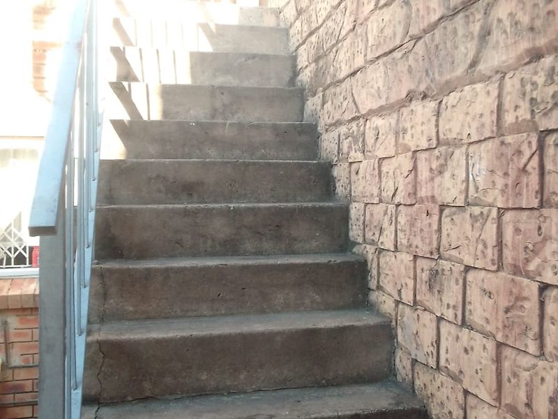 An exterior concrete staircase featuring a metal handrail and stone cladding wall, showing signs of weathering and structural wear.