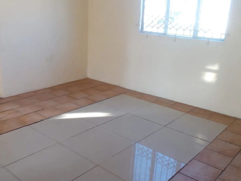 An empty bedroom featuring mismatched floor tiles and a window fitted with security bars, offering a blank canvas for renovation.
