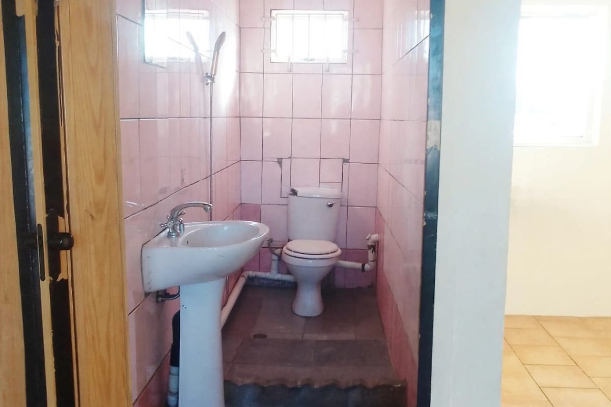 A compact bathroom featuring a pedestal basin and toilet with dated pink wall tiles and exposed plumbing, requiring modernization.