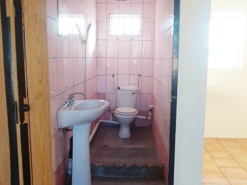 A compact bathroom featuring a pedestal basin and toilet with dated pink wall tiles and exposed plumbing, requiring modernization.