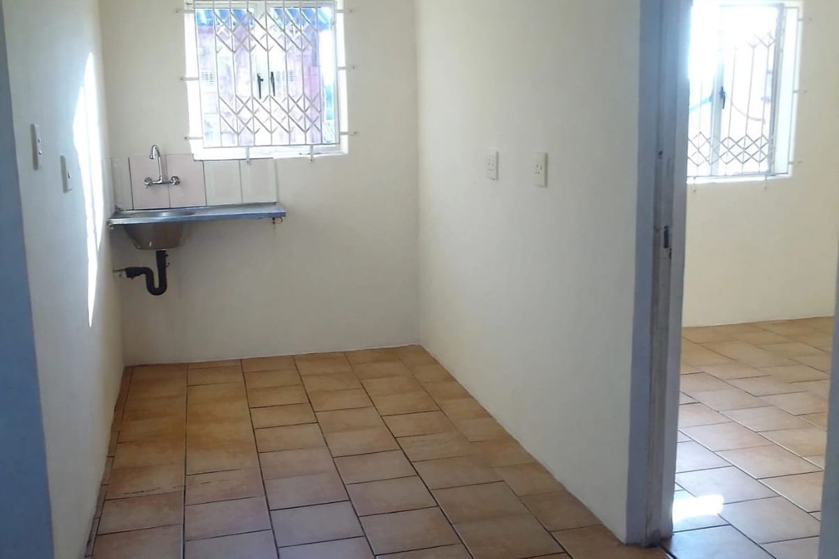 A compact, empty kitchen area featuring tiled flooring, a wall-mounted stainless steel sink, and security bars on the windows.