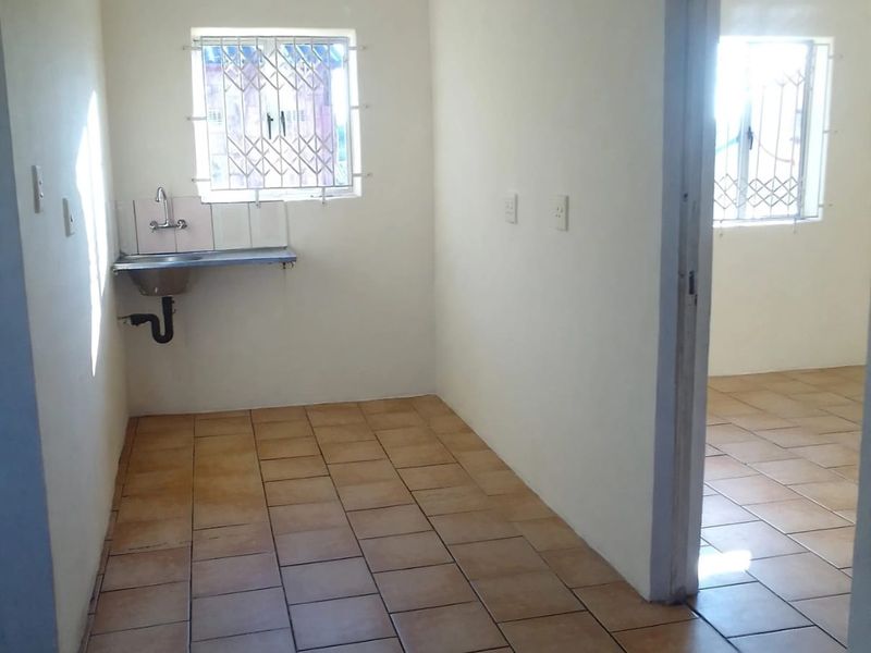 A compact, empty kitchen area featuring tiled flooring, a wall-mounted stainless steel sink, and security bars on the windows.