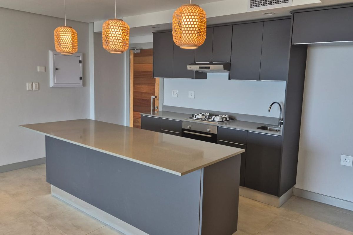 Modern kitchen featuring a central island, quartz countertops, built-in gas hob, oven, extractor fan, and sleek dark cabinetry with integrated storage.