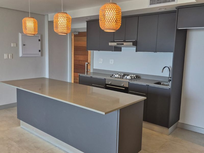 Modern kitchen featuring a central island, quartz countertops, built-in gas hob, oven, extractor fan, and sleek dark cabinetry with integrated storage.