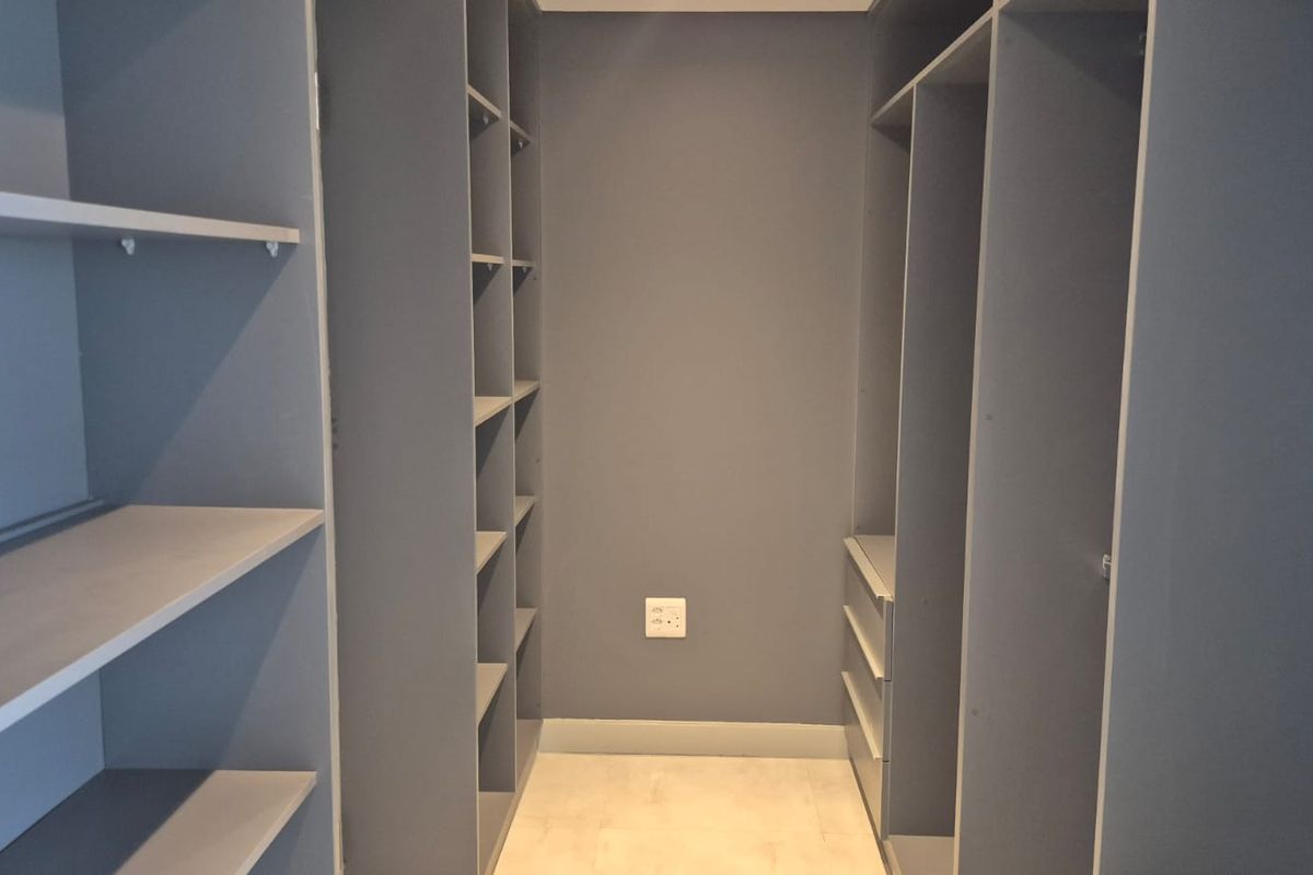 A walk-in closet or dressing area featuring extensive built-in grey cabinetry with open shelving and integrated drawers.