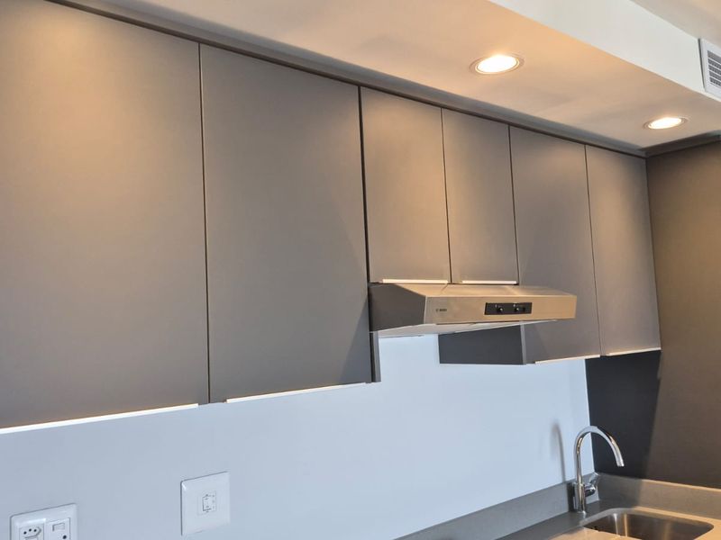 Modern kitchen featuring sleek grey cabinetry, integrated extractor fan, stainless steel sink with mixer tap, and recessed ceiling lighting.