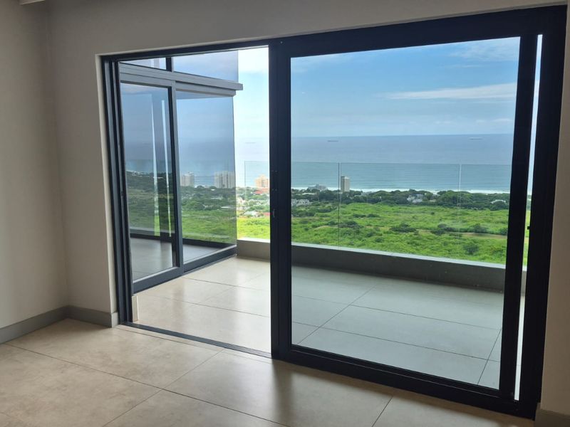 Bright and spacious living area featuring large sliding glass doors that open onto a balcony with expansive ocean and coastal views.
