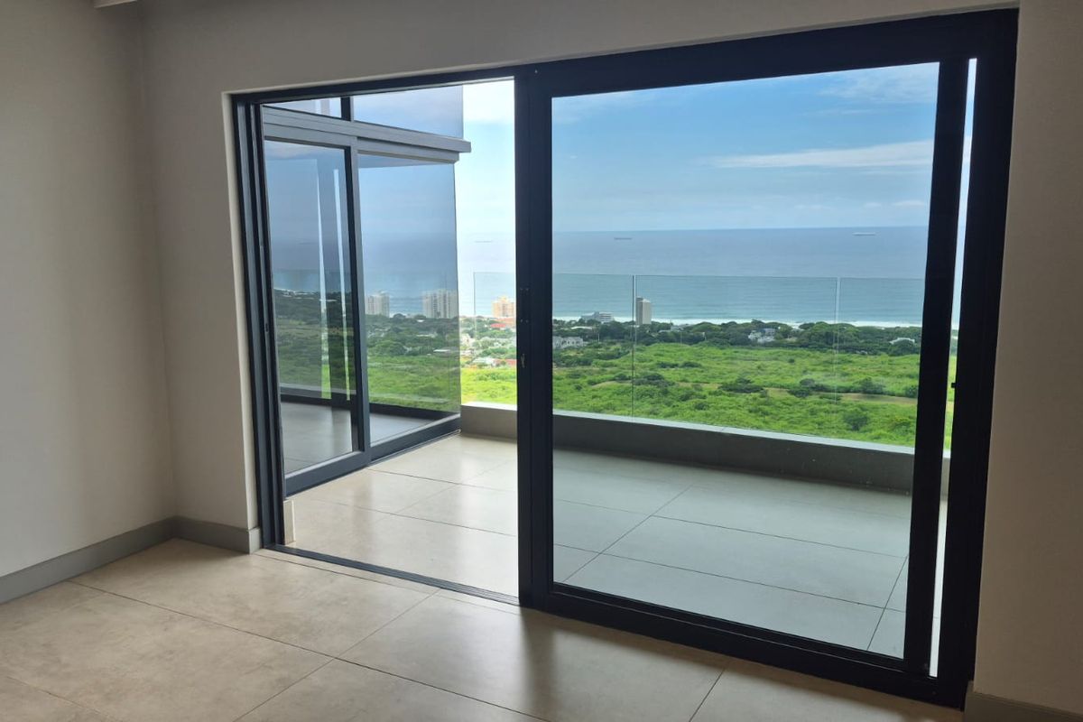 Bright and spacious living area featuring large sliding glass doors that open onto a balcony with expansive ocean and coastal views.