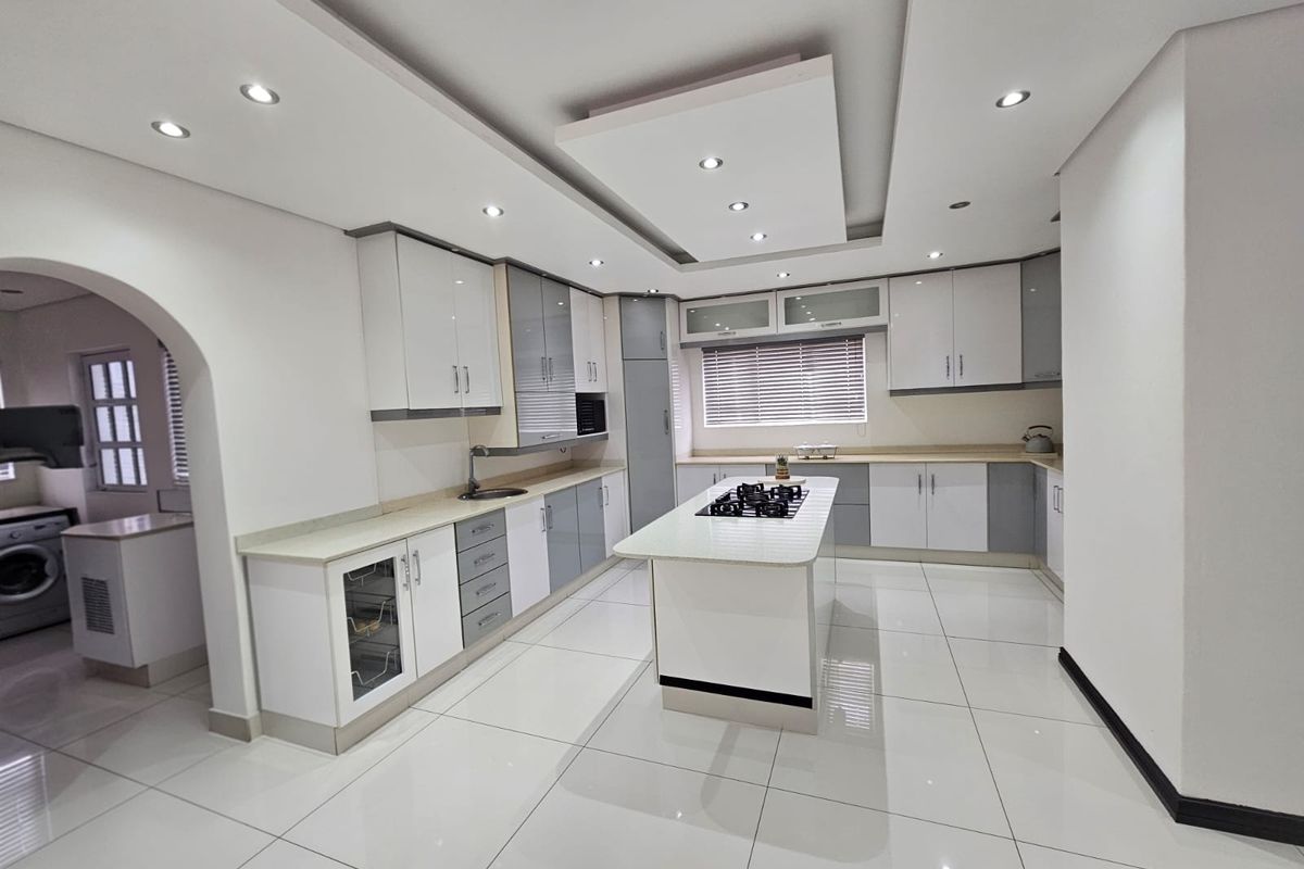 Modern kitchen featuring a central island with a gas hob, sleek white and grey cabinetry, recessed ceiling lighting, and polished tiled flooring.