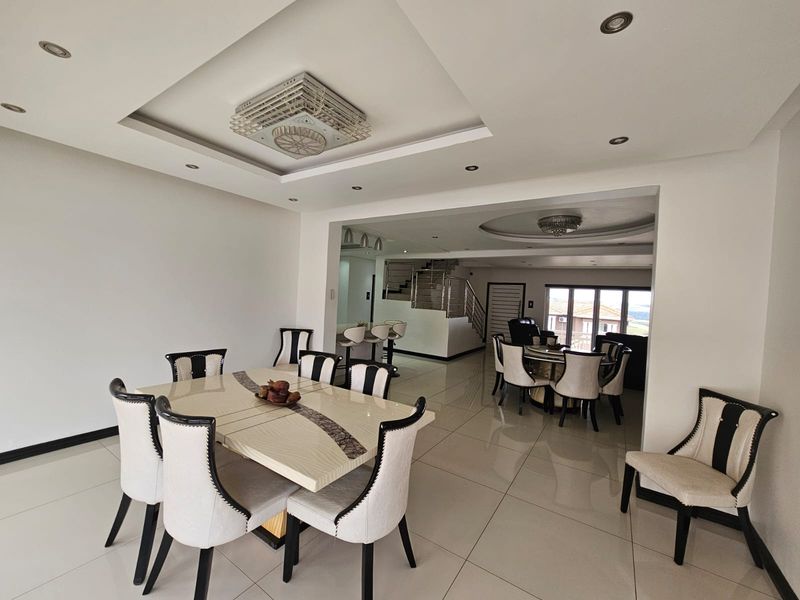 Spacious open-plan living and dining area featuring polished porcelain floor tiles, modern recessed ceiling lighting, and a contemporary staircase with metal balustrades.