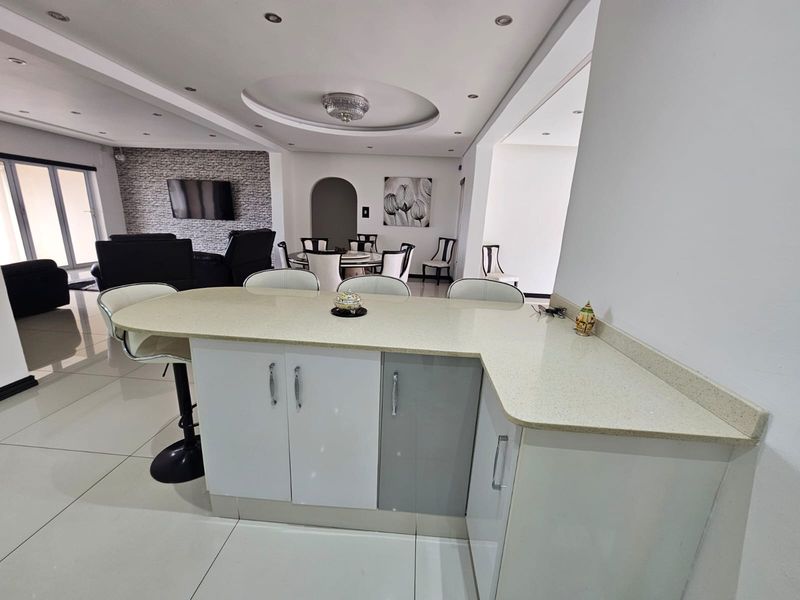 Spacious open-plan living area featuring a modern kitchen island with stone countertops, tiled flooring, and a decorative coffered ceiling with recessed lighting.